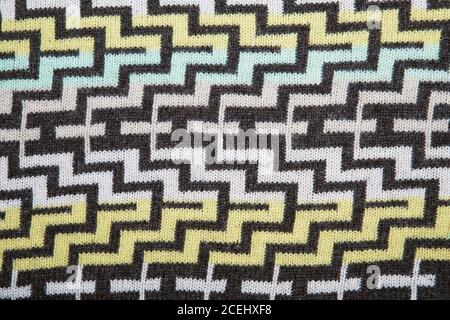Ein geometrisches Muster auf einem Strickstoff. Weihnachtliche Zierstrick. Gestrickter Pullover im Hintergrund. Echt gestrickt Stoff texturierter Hintergrund Stockfoto