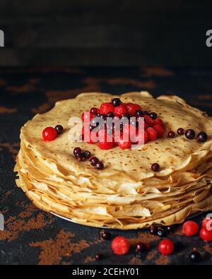 Russische Pfannkuchen mit Beeren vor dunklem Hintergrund. Pancake Week - das alte slawische Fest des Sehens aus dem Winter, von dem der Brauch Stockfoto