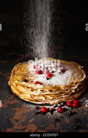 Russische Pfannkuchen mit Beeren bestreut mit Zuckerpulver vor dunklem Hintergrund. Pancake Week - das alte slawische Fest des Sehens aus dem wi Stockfoto