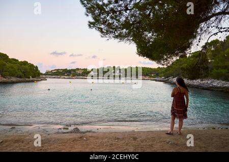 Frau am Strand von Caló des Homes Morts bei Sonnenuntergang mit Villen im Hintergrund (Santanyí, Mallorca, Balearen, Mittelmeer, Spanien) Stockfoto