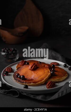 Gesundes Sommerfrühstück, hausgemachte klassische amerikanische Pfannkuchen mit frischen Beeren, Nüssen und Honig auf dunklem Hintergrund. Dunkle und launische Food-Fotografie Stockfoto