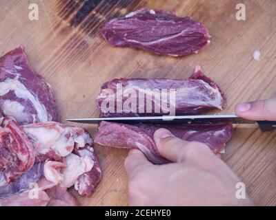 Die Hände der anonymen Person, die das frische rohe Fleisch auf hölzern schneidet Tabelle Stockfoto