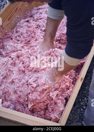 Unbekanntes Männchen, das rohes Hackfleisch mit Händen in Holz mischt Trog Stockfoto