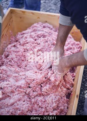 Unbekanntes Männchen, das rohes Hackfleisch mit Händen in Holz mischt Trog Stockfoto