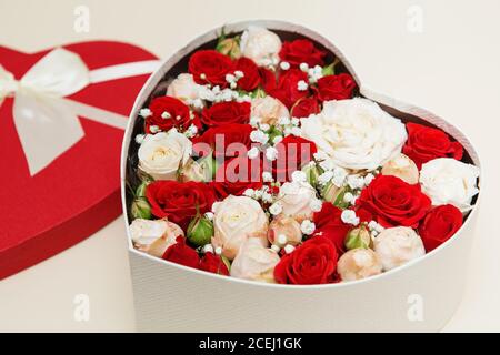 Rote und weiße Rosen in einer weißen Box im Form eines Herzens auf einem warmen weißen Hintergrund Stockfoto