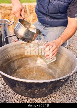 Unkenntlich Mann Gießen frisches sauberes Wasser in Glas, während Sitzen in der Nähe Kessel im Hof Stockfoto