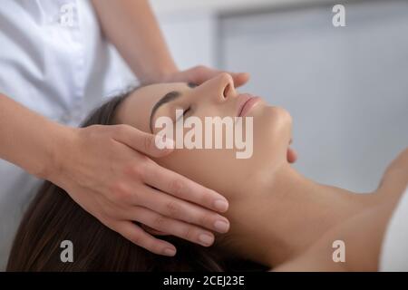 Junge hübsche Frau liegend und mit Gesichtsmassage Stockfoto