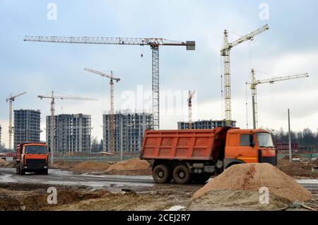 Schwere Muldenkipper und hydraulische Wippauslegerkrane arbeiten auf einer Baustelle. Turmdrehkran baut ein neues Wohngebäude. Gruppe von Towe Stockfoto