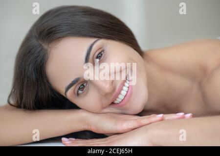 Junge Frau, die sich auf einer Couch niederlegt und freundlich lächelt Stockfoto