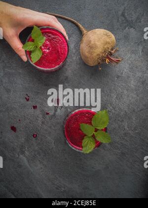 Frau Hand hält Glas Rote Beete Smoothie mit Minzblättern auf dunklem Tisch. Overhead-Aufnahme mit Kopierplatz. Stockfoto