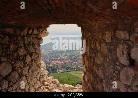 Blick auf das Dorf Pavlov aus dem Fenster der Ruinen der Burg Devicky in Palava Landschaftsschutzgebiet. Felsenfenster mit Blick auf das ländliche Dorf. Stockfoto