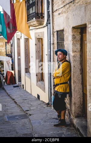 MITTELALTERLICHER MARKT - PUEBLA DE SANABRIA - ZAMORA - SPANIEN - AGOUST 13, 2017: Nachdenklicher erwachsener Mann in traditionellem historischen Anzug, der sich auf das Gebäude stützt und wegschaut Stockfoto