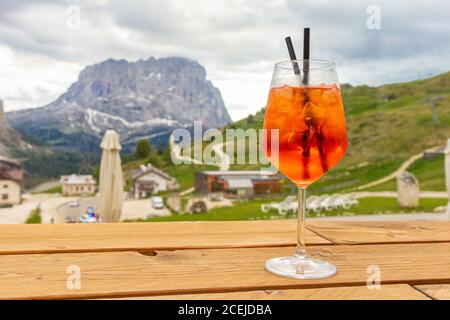 Blick auf das traditionelle italienische Alkoholgetränk Aperol Spritz auf den Hintergrund von bunten italienischen Wiesen und den Dolomiten Alpen. Dorf Stockfoto