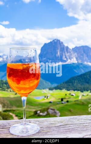 Blick auf das traditionelle italienische Alkoholgetränk Aperol Spritz auf den Hintergrund von bunten italienischen Wiesen und den Dolomiten Alpen. Dorf Stockfoto