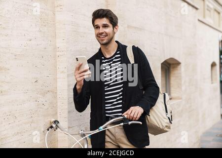 Bild von einem jungen gut aussehend zufrieden lächelnden Geschäftsmann im Freien Mit dem Smartphone auf dem Fahrrad Stockfoto