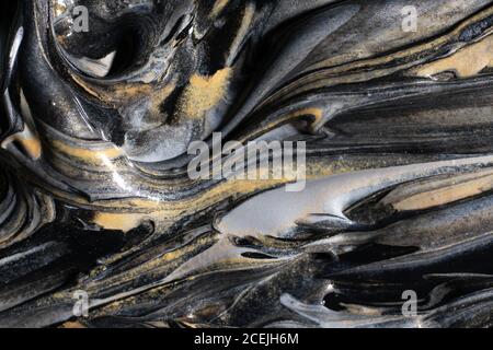 Verschüttete glänzende goldene und silberne Farbstoffe mischen sich mit schwarz Pigment Stockfoto