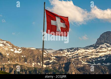 Die Schweizer Flagge weht auf dem Bühlberg über Lenk im Berner Oberland, Schweiz, vor dem Kamm, der den Kanton Bern vom Wallis trennt. Mit 1.664 Metern betreiben Anja und Gunter Steininger dort das Bergrestaurant Bühlberg, eine Dependance des Hotel Lenkerhof. Stockfoto