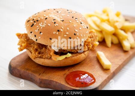 Hausgemachter Chicken Strips Burger mit Pommes Frites und sauer-süßer Sauce auf rustikalem Brett, Seitenansicht. Stockfoto