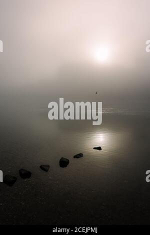 Felsen im See zwischen Nebel und Vogel fliegen über Wasser Oberfläche Stockfoto