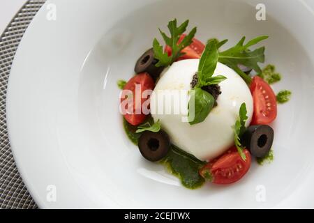 Traditionelle authentische weiche und cremige frische italienische Burrata Käse geformt Als weiße runde Kugel über italienischen Tomaten mit Rucola gekrönt Entlang der Seite Stockfoto
