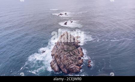 Malerische Drohne Blick auf das Meer Wasser planscht um kleine Klippe in Asturien, Spanien Stockfoto