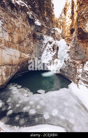 Fluss läuft in geschmolzenem Hochlandsee bei verschneiten Spalten mit Braune Felsen und einige Wintertannen an sonnigen Tagen Stockfoto