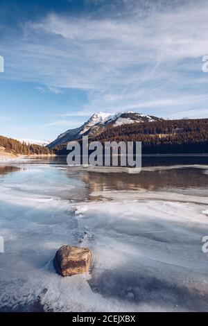 Fluss läuft in geschmolzenem Hochlandsee bei verschneiten Spalten mit Braune Felsen und einige Wintertannen an sonnigen Tagen Stockfoto