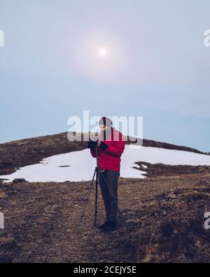Junge Bart Kerl in Skijacke Befestigung Kamera auf Stativ†field Und Sonnenschein am blauen Himmel in Island Stockfoto