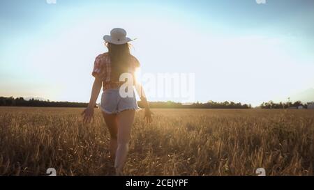 Glückliche Frau läuft auf einem Weizenfeld mit offenen Armen bei Sonnenuntergang. Stockfoto