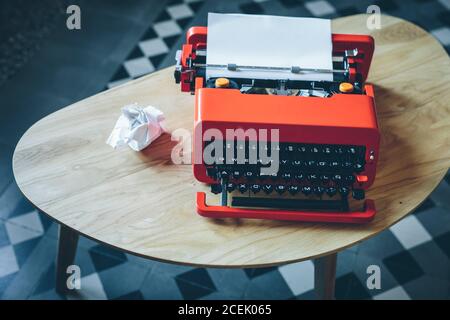 Knallrote Schreibmaschine mit eingelegtem und zerknittertem Papier Auf einem kleinen Tisch Stockfoto