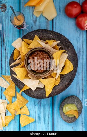 Von oben Blick auf Nachos Teller mit Sauce in der Mitte Und Tomaten mit Käse in der Nähe auf hölzernen Hintergrund gelegt Stockfoto