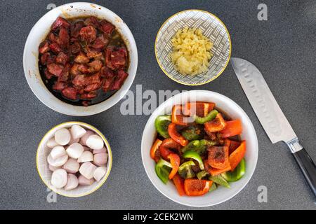 Vorbereitete gehackte Rohzutaten - Rindfleisch, Paprika, Zwiebeln, Knoblauch und Ingwer in Schüsseln mit einem japanischen Messer bereit für das Kochen einer Rührfritte Gericht Stockfoto