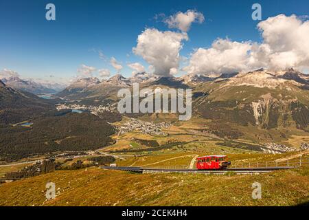 Die rote Muottas-Muragl-Seilbahn fährt auf ihrer Schiene durch das Bergpanorama des Engadins, Graubünden, Schweiz. Im Tal liegen die Städte Pontresina, Celerina, St. Moritz und im Hintergrund Silvaplana. Stockfoto