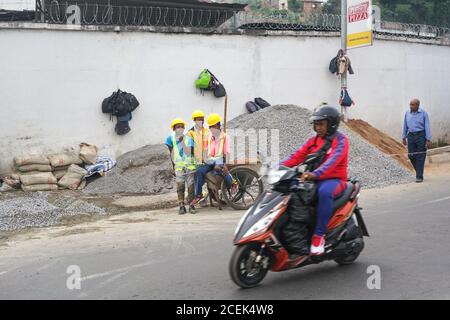 Antananarivo, Madagaskar - 24. April 2019: Unbekannte madagassische Arbeiter in Hüten und reflektierenden Jacken stehen in der Nähe von Kieshaufen auf der Baustelle Stockfoto