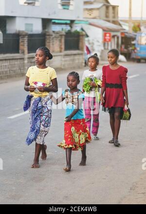 Ranohira, Madagaskar - 29. April 2019: Gruppe von vier unbekannten jungen madagassischen Mädchen in bunten Kleidern, die am Abend barfuß auf der m laufen Stockfoto