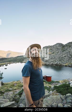 Junger Mann, der in der Nähe des Sees mit einem Becher steht Stockfoto