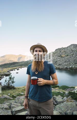 Junger Mann, der in der Nähe des Sees mit einem Becher steht Stockfoto