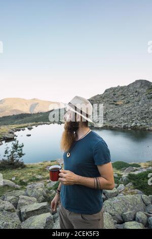 Junger Mann, der in der Nähe des Sees mit einem Becher steht Stockfoto