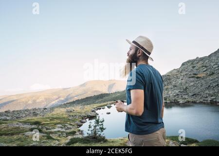 Junger Mann, der in der Nähe des Sees mit einem Becher steht Stockfoto