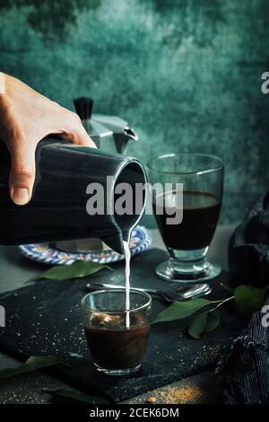 Frau, die Milch in einem Glas Kaffee serviert Stockfoto