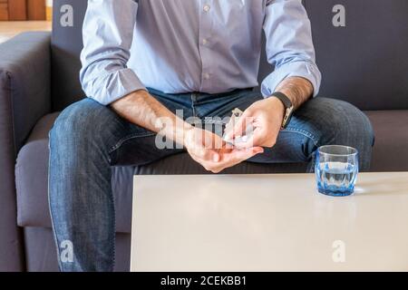 Der Mensch nimmt Pillen trinkt ein Glas Wasser und sitzt Auf dem Sofa in seinem Wohnzimmer Stockfoto