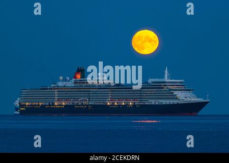 Weymouth, Dorset, Großbritannien. September 2020. Wetter in Großbritannien. Der volle Maismond erhebt sich hinter dem Cunard-Kreuzfahrtschiff Queen Elizabeth, das vor der Küste von Weymouth in Dorset vor Anker liegt. Traditionell ist der September der Erntemond, aber in diesem Jahr wird es Anfang Oktober sein, da er dem Herbst-Tagundnachtgleiche am nächsten kommt. Bild: Graham Hunt/Alamy Live News Stockfoto