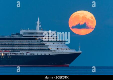 Weymouth, Dorset, Großbritannien. September 2020. Wetter in Großbritannien. Der volle Maismond erhebt sich hinter dem Cunard-Kreuzfahrtschiff Queen Elizabeth, das vor der Küste von Weymouth in Dorset vor Anker liegt. Traditionell ist der September der Erntemond, aber in diesem Jahr wird es Anfang Oktober sein, da er dem Herbst-Tagundnachtgleiche am nächsten kommt. Bild: Graham Hunt/Alamy Live News Stockfoto