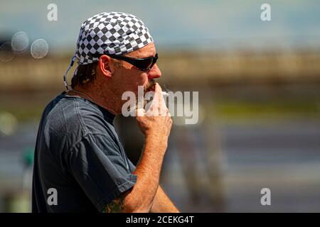 Chestertown, MD, USA 08/30/2020: Profilbild eines kaukasischen Rockers mittleren Alters mit Schachbrettmuster-Bandanna und Sonnenbrille ist rauchig Stockfoto