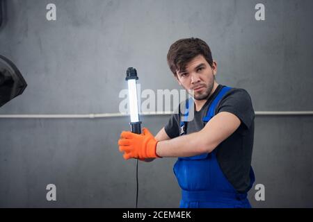 Ein Arbeiter in blauen Overalls und Arbeitshandschuhe hält ein Taschenlampe Stockfoto