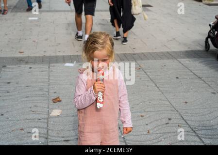 Blonde kleine Mädchen essen ein Eis auf der Straße in Santander, Kantabrien, Spanien während der Stadt Fest. Juli 2019 Stockfoto