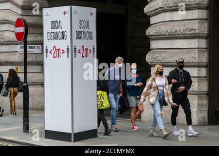 London, Großbritannien. August 2020. Mitglieder der Öffentlichkeit tragen Gesichtsmasken gehen an einem "Social Distanzing" Zeichen an Regents Street während Coronavirus Pandemie.Es ist obligatorisch, Gesichtsmasken während der Reise zu tragen. Kredit: SOPA Images Limited/Alamy Live Nachrichten Stockfoto