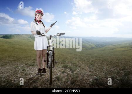 Asiatische Frau mit einem Fahrradhelm neben ihrem Fahrrad stehen Auf dem Wiesenfeld Stockfoto