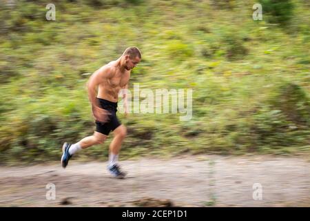 Sportler läuft bergauf im Hintergrund Bergfluss, Berge und Wald. Sprint-Rennen. Schnelle Bewegungen und Laufeffekte, Unschärfe Stockfoto