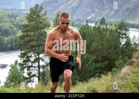 Sportler läuft bergauf im Hintergrund Bergfluss, Berge und Wald. Sprint-Rennen. Schnelle Bewegungen und Laufeffekte, Unschärfe Stockfoto
